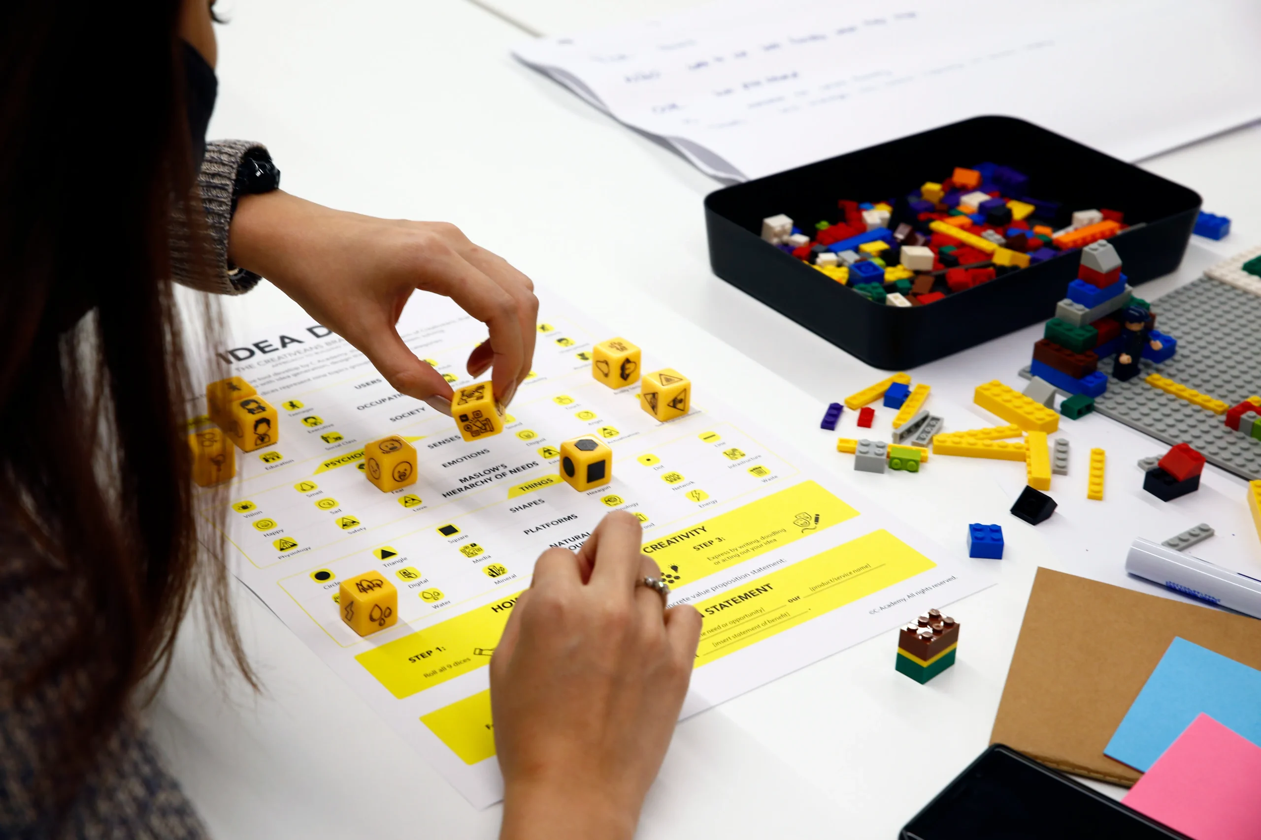 Person placing yellow dice on a bright worksheet during a hands-on activity, with colorful LEGO bricks nearby.
