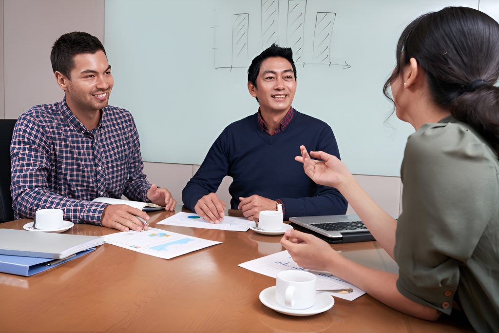 Three colleagues having a discussion during a meeting around a conference table with documents and coffee cups.