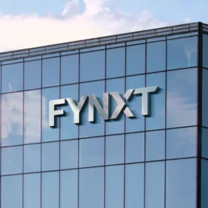 Silver 3D "FYNXT" logo mounted on the reflective glass facade of a modern office building exterior.