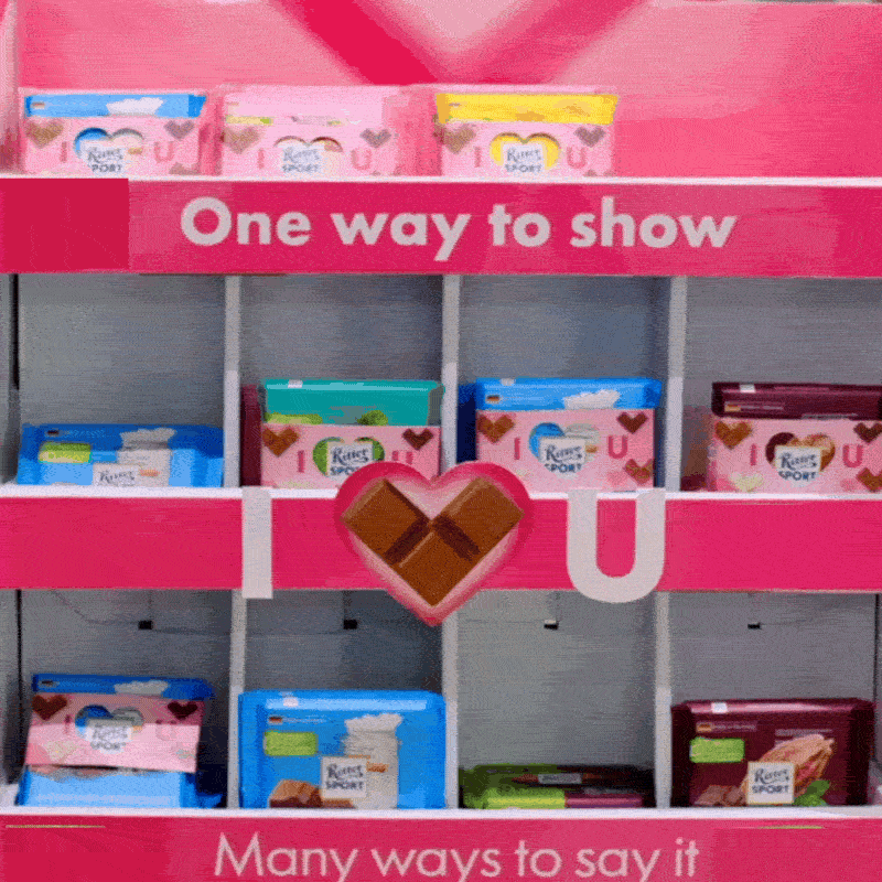 A pink Ritter Sport promotional display stand in a store showcasing various chocolate bars organized by flavor on its shelves.