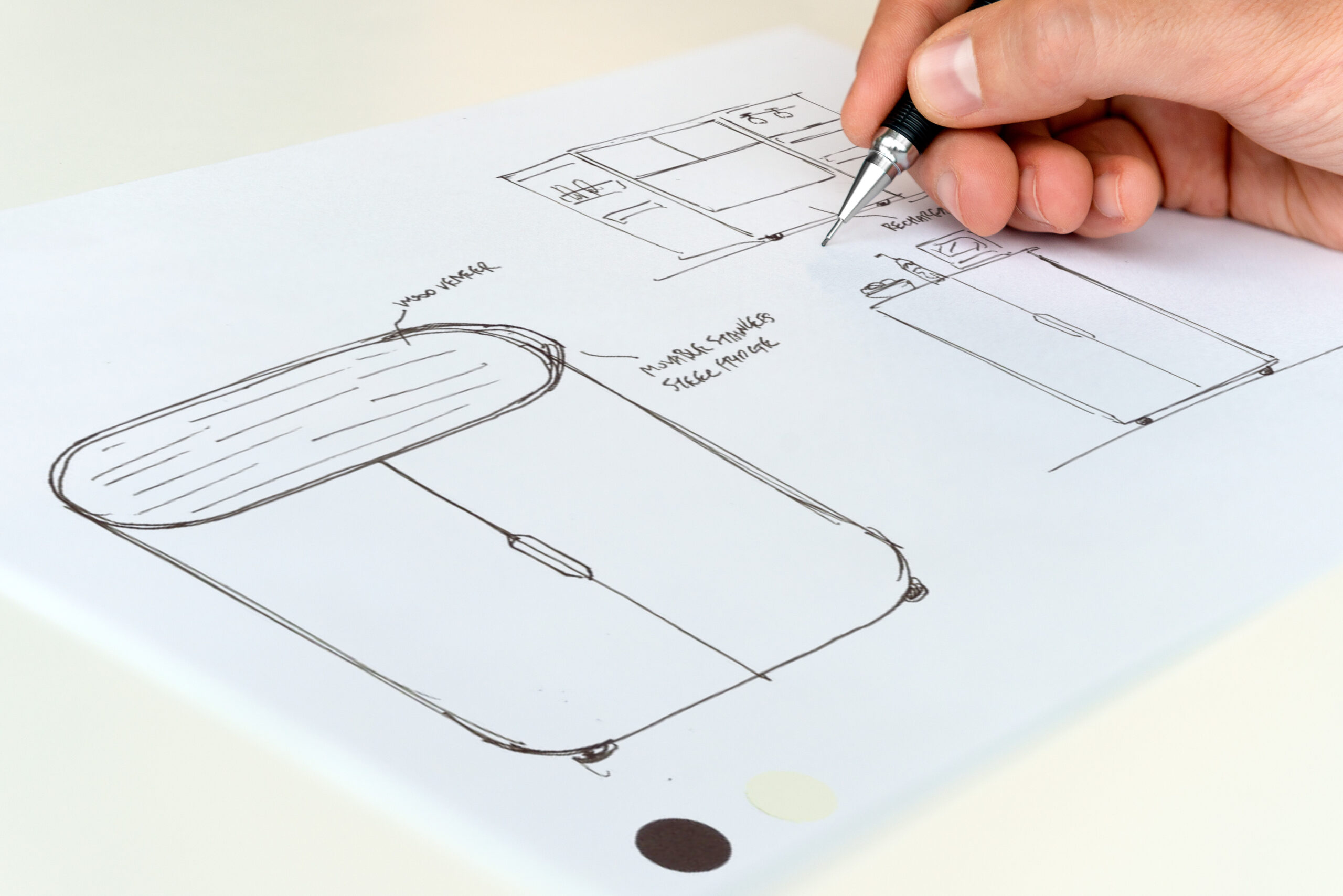 A hand holding a mechanical pencil sketching furniture concepts and product details on a white sheet of paper.