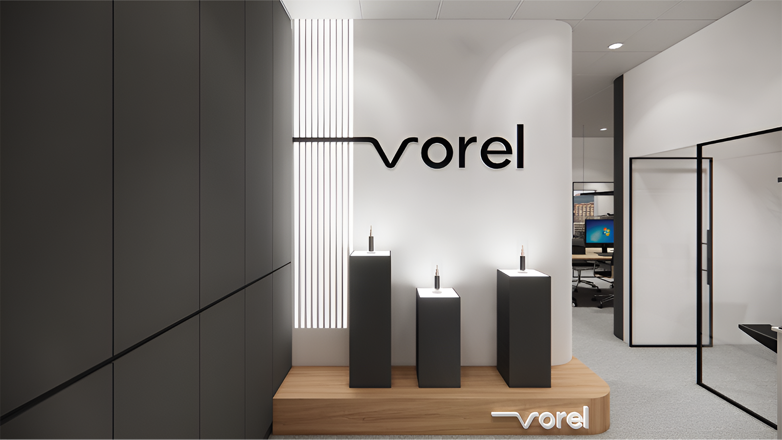 Modern corporate showroom featuring three black pedestals displaying products on a wooden platform, beneath a white feature wall with black Vorel logo signage.