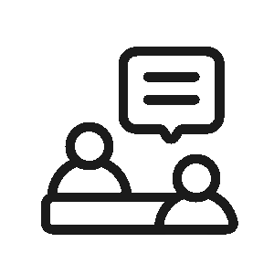 A black line icon depicting two simplified human figures sitting across a table from one another, with a speech bubble containing text lines appearing above them to represent communication or a consultation, set on a transparent grid background.